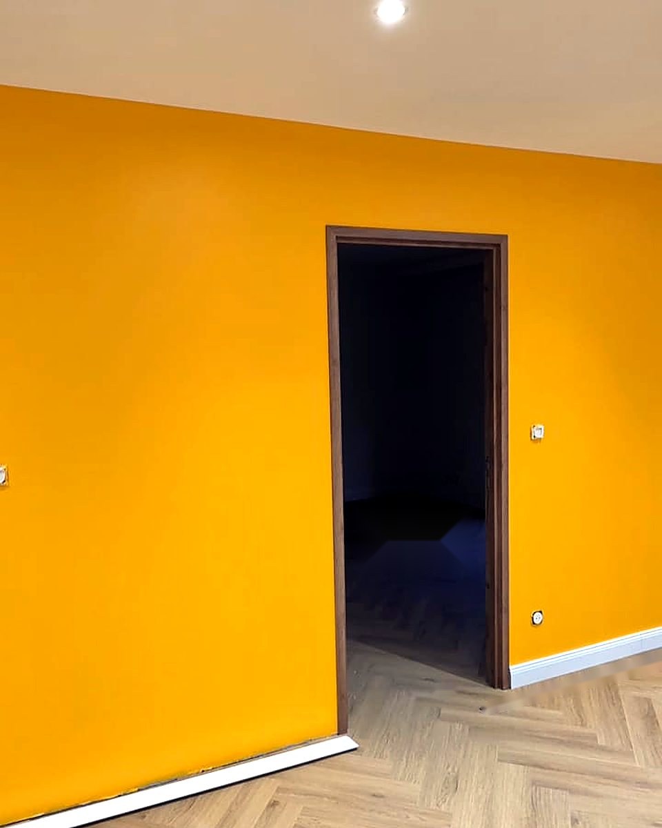 Pièce de vie avec mur d'accent jaune, portes bois et parquet à chevrons